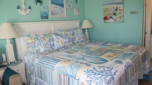 A bedroom with a bed covered in a blue and white patterned bedspread, a white nightstand with a lamp, and wall decorations including a framed picture and a sign. - Bogue Shores, King bed. Pool side, Beach and Sound Access-sleeps 4 (Atlantic Beach)
