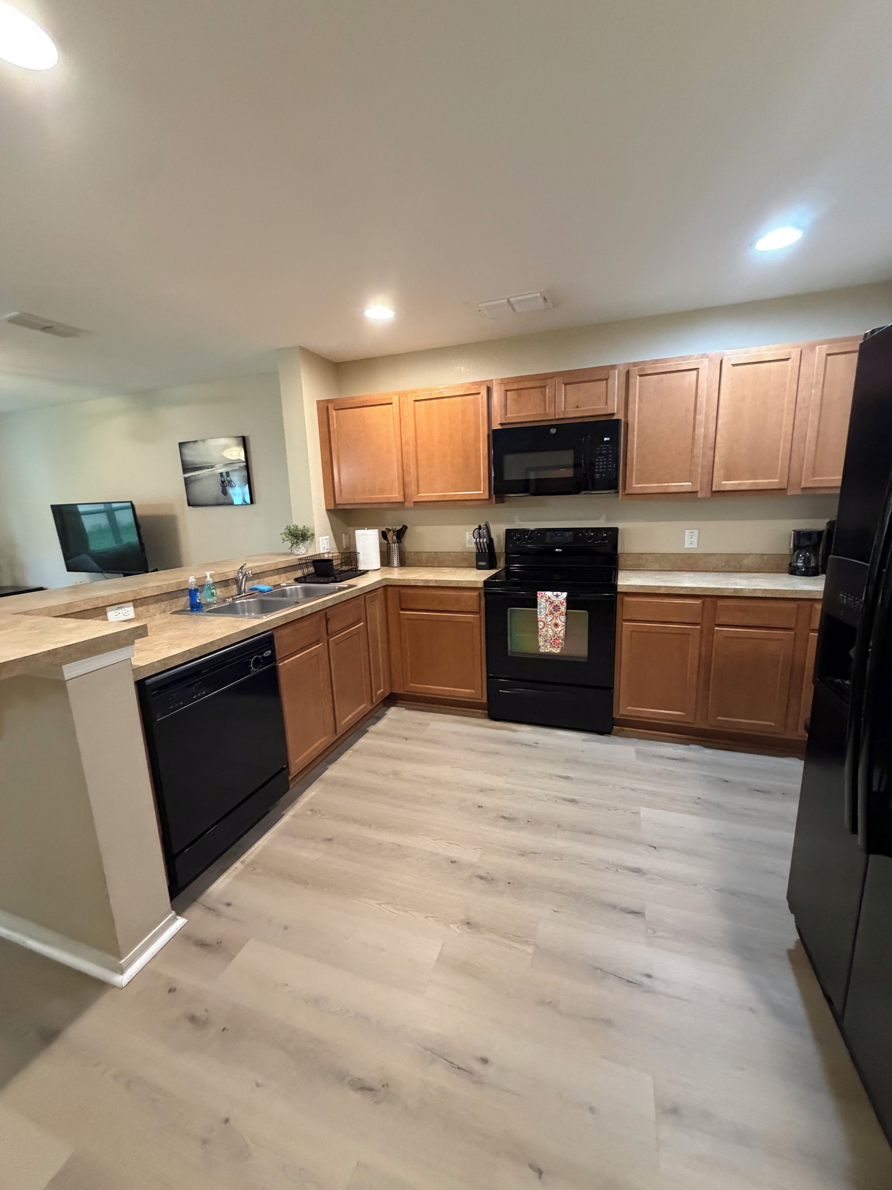 A modern kitchen with wooden cabinets, a black microwave, a stove, and a dishwasher.