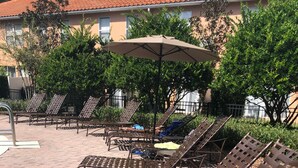 Espace extérieur aménagé avec des chaises et des tables en métal, un grand parasol et un bâtiment en arrière-plan.