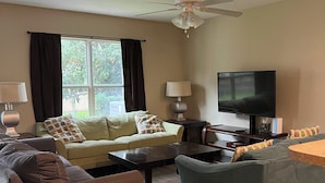 Un salon comprenant un canapé, des fauteuils, une table basse, un téléviseur et un ventilateur de plafond.