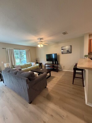 A living room with a sofa, coffee table, TV, and a ceiling fan.
