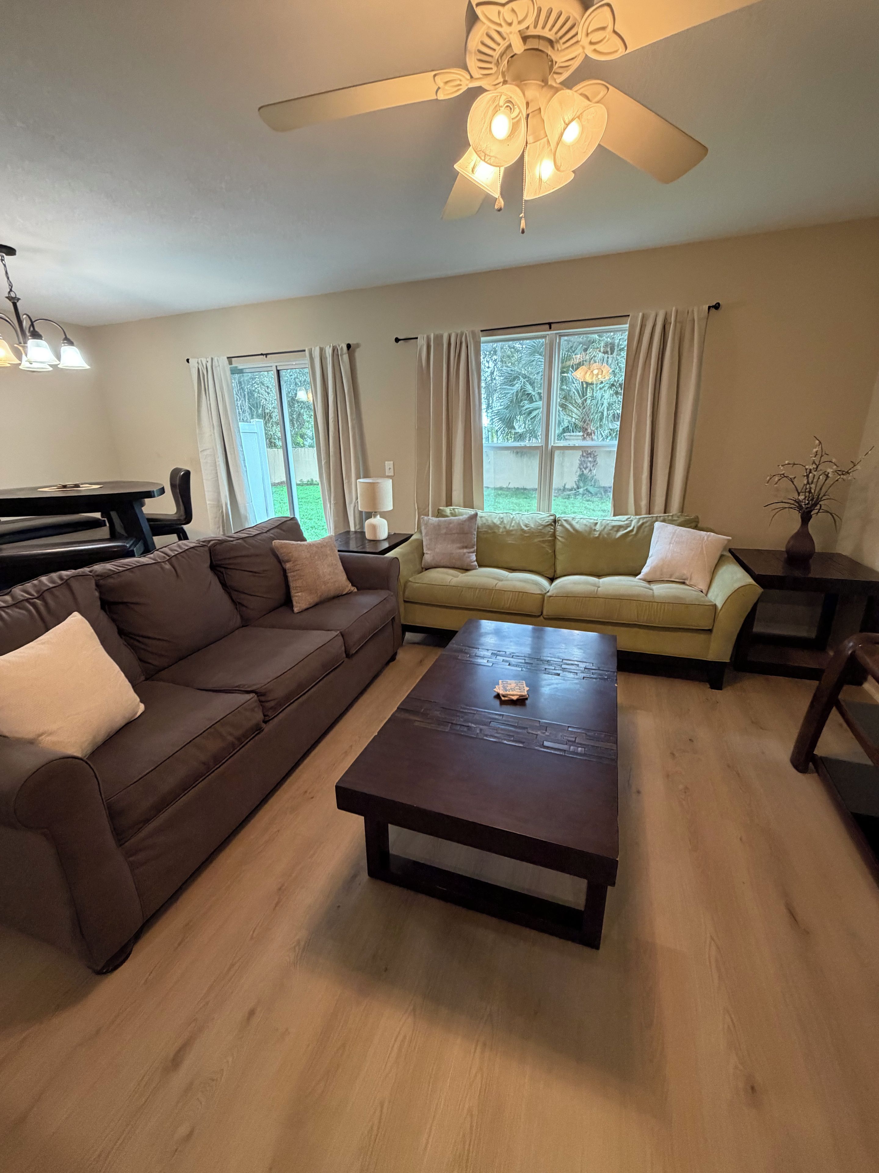 A living room with a brown sofa, a yellow sofa, a wooden coffee table, and a ceiling fan.
