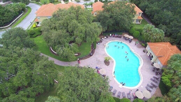 Vue aérienne d’un quartier résidentiel avec une piscine entourée d’une végétation luxuriante et de quelques maisons.