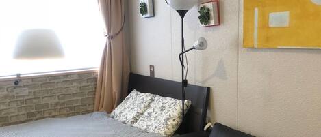 A room with a bed, a black leather sofa, a wooden table with plants, a floor lamp, and a wall-mounted air conditioner.