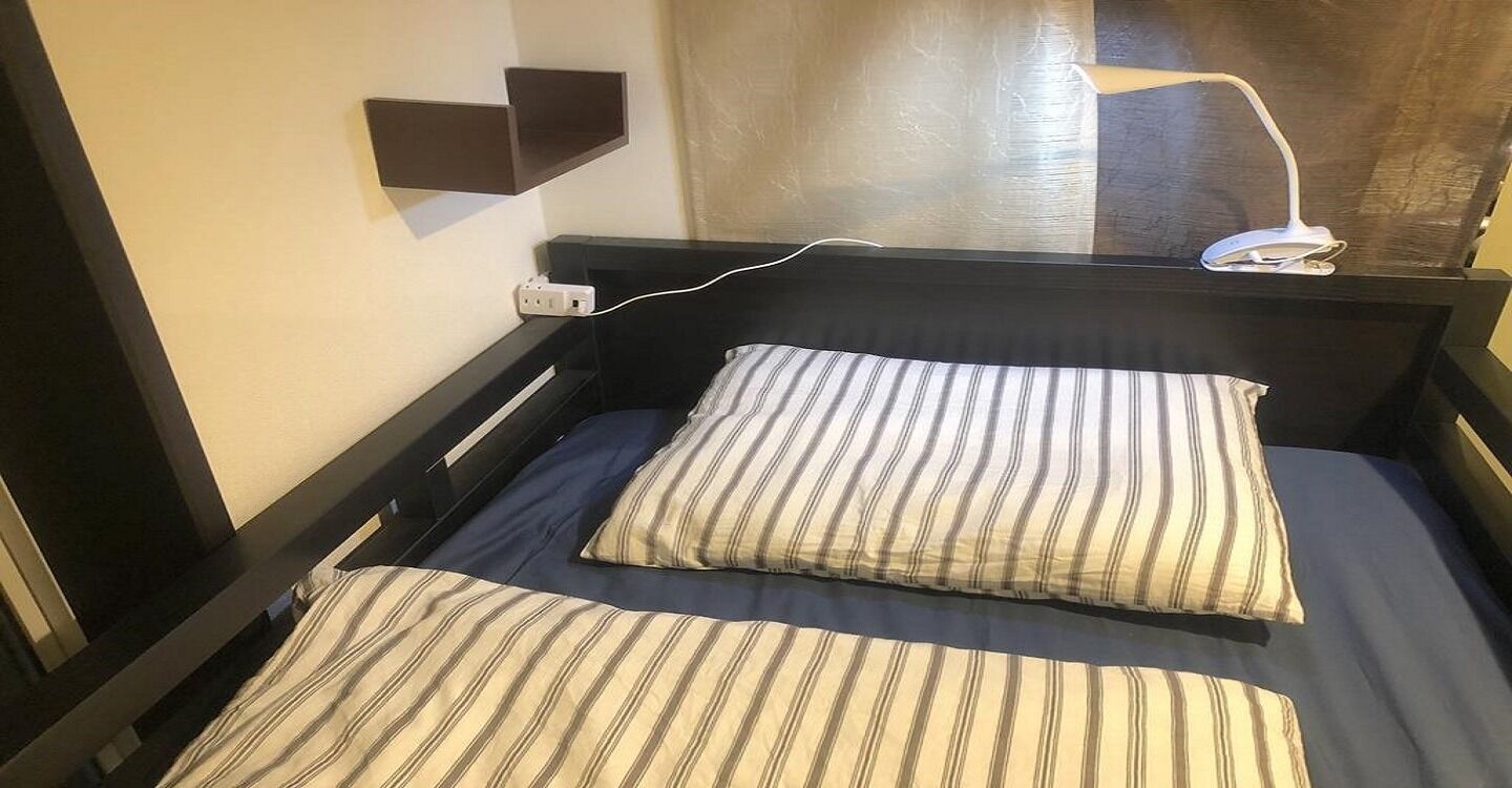 A single bed with striped bedding, a bedside table, a wall-mounted lamp, and a power outlet.