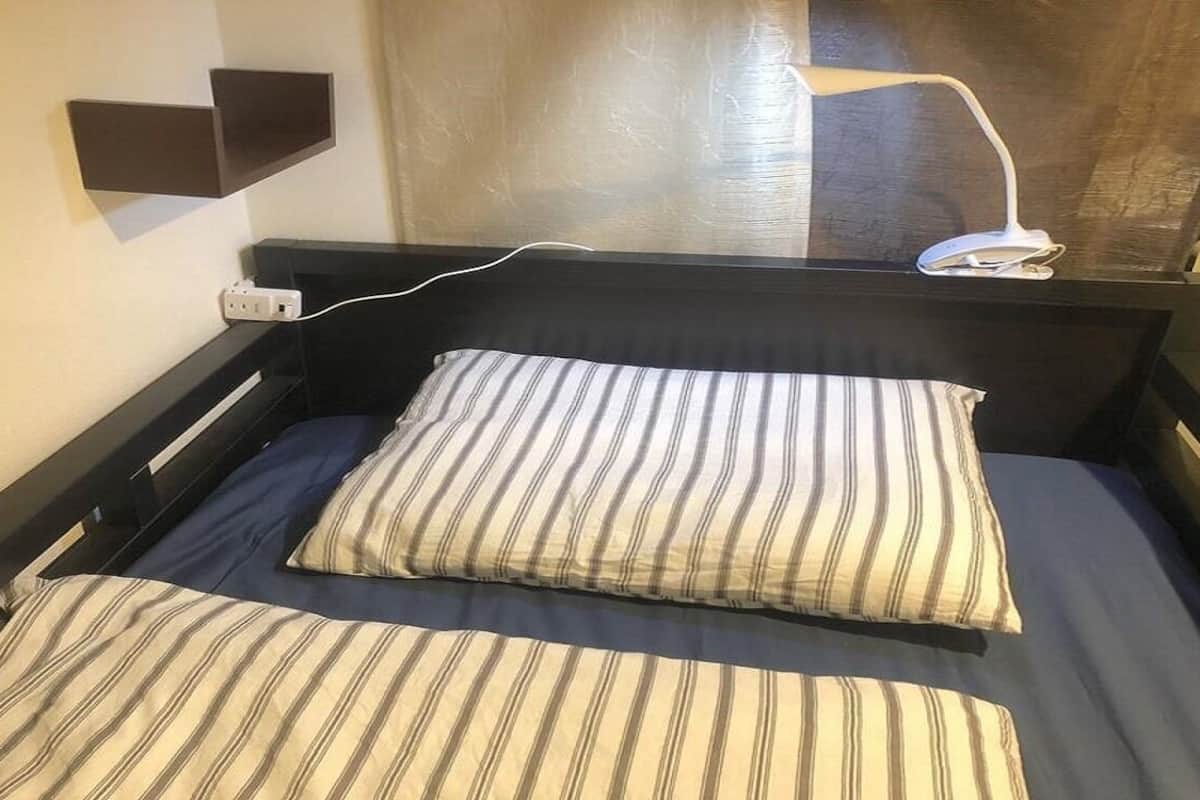 Una cama individual con ropa de cama a rayas, una mesita de noche, una lámpara de pared y un enchufe.