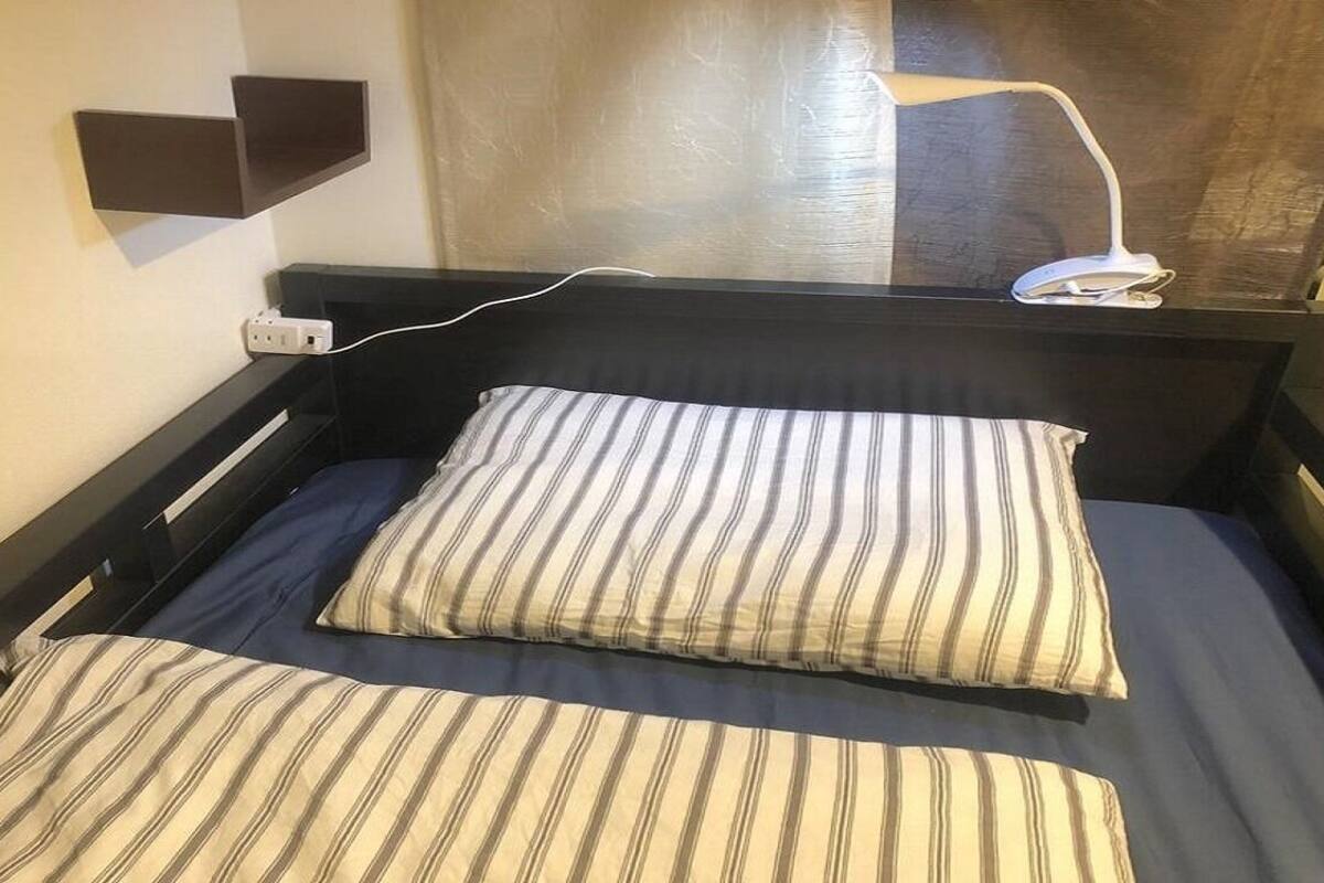 A single bed with striped bedding, a bedside table, a wall-mounted lamp, and a power outlet.