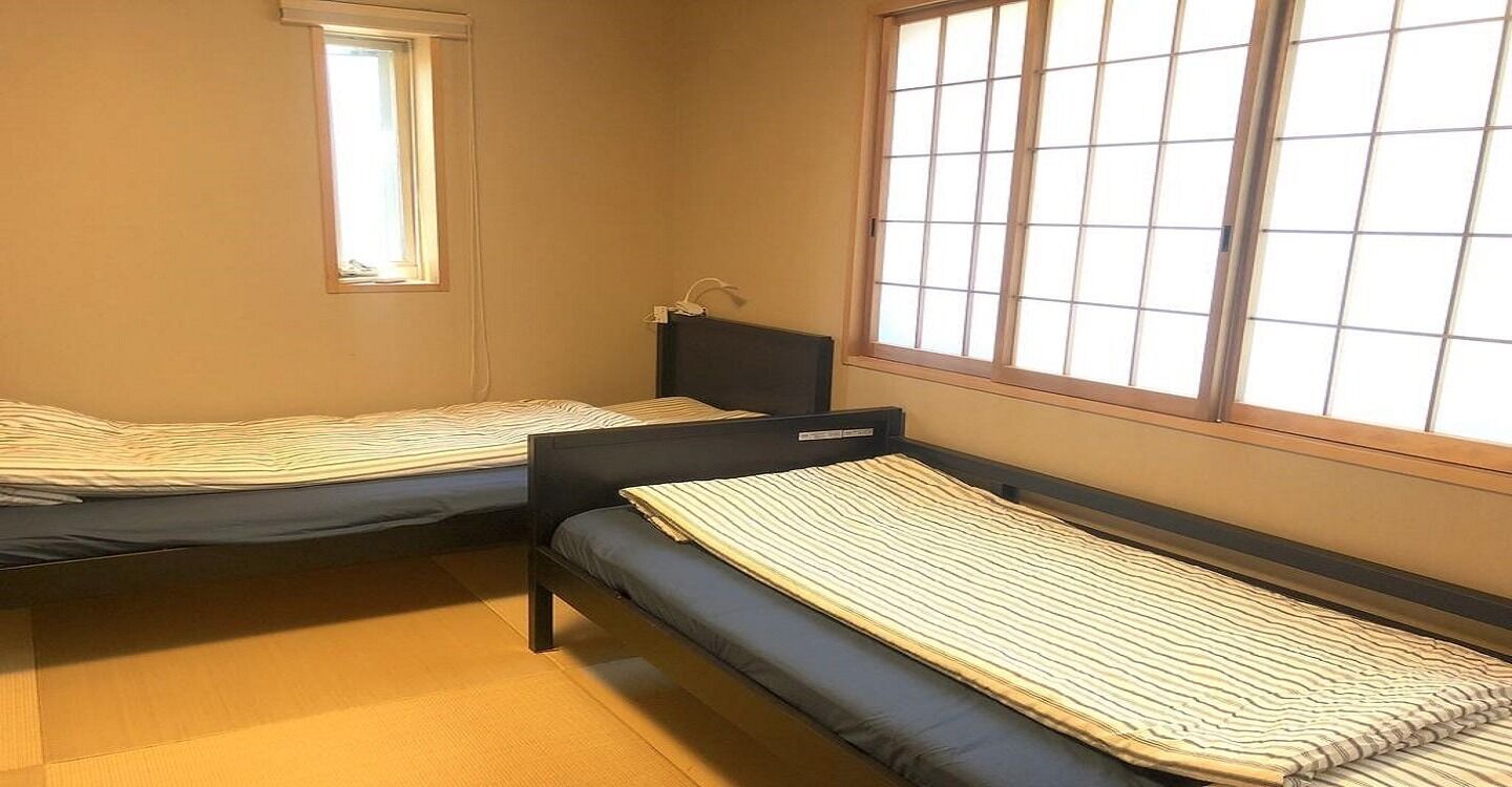 Two single beds with headboards, a window with blinds, and a small bedside table.