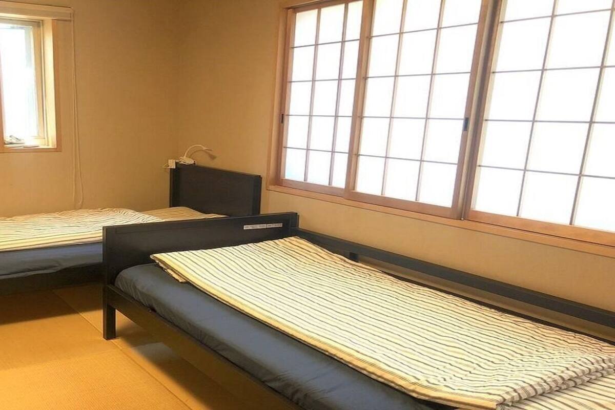 Two single beds with headboards, a window with blinds, and a small bedside table.