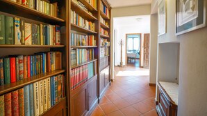 Een gang met houten boekenkasten vol boeken, die uitkomt op een eetgedeelte met een tafel en stoelen.