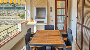 Een balkon met rieten meubilair, een houten tafel en een stenen muur.