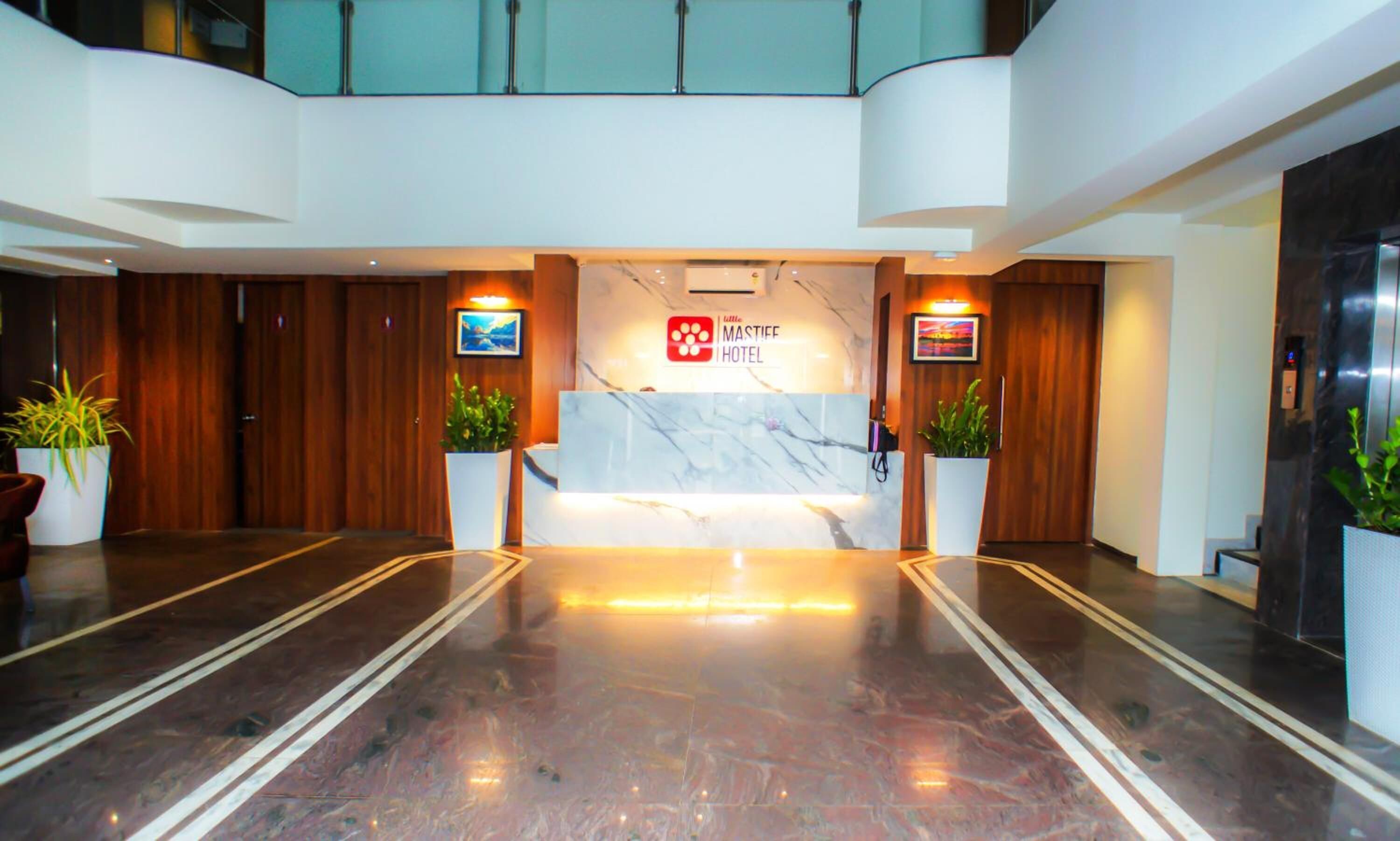 A hotel reception area with a marble counter, wooden paneling, and potted plants.