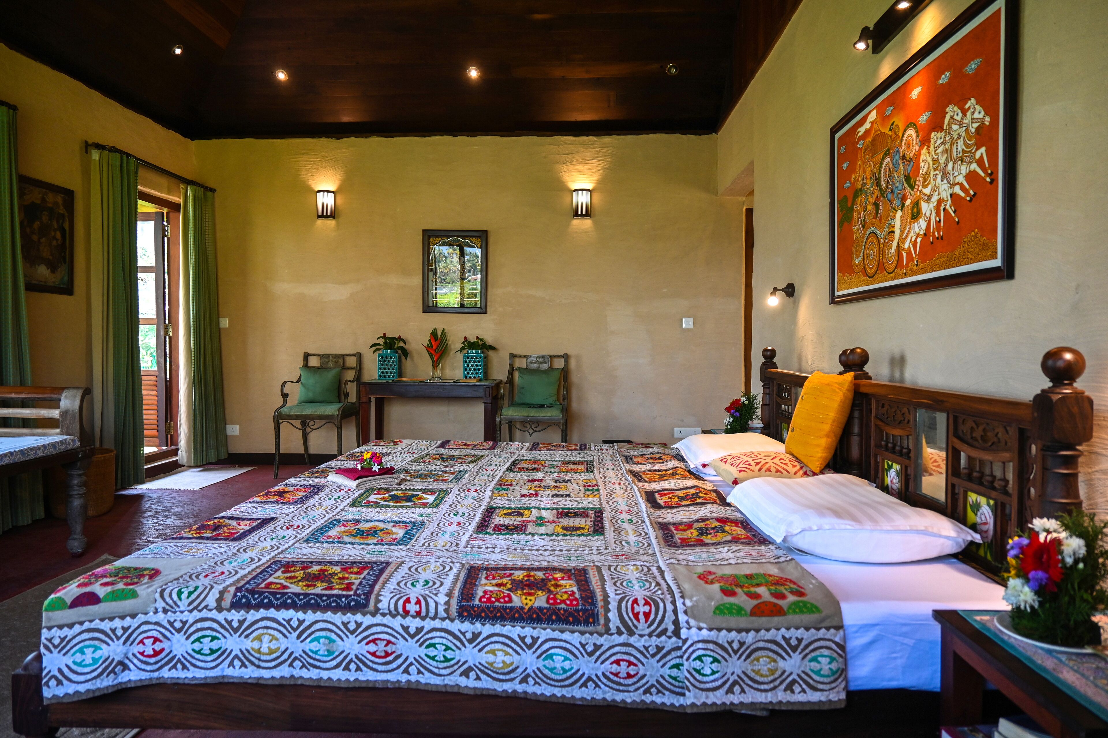 A bedroom with a large bed, a wooden headboard, a green chair, a small table, and a painting on the wall.