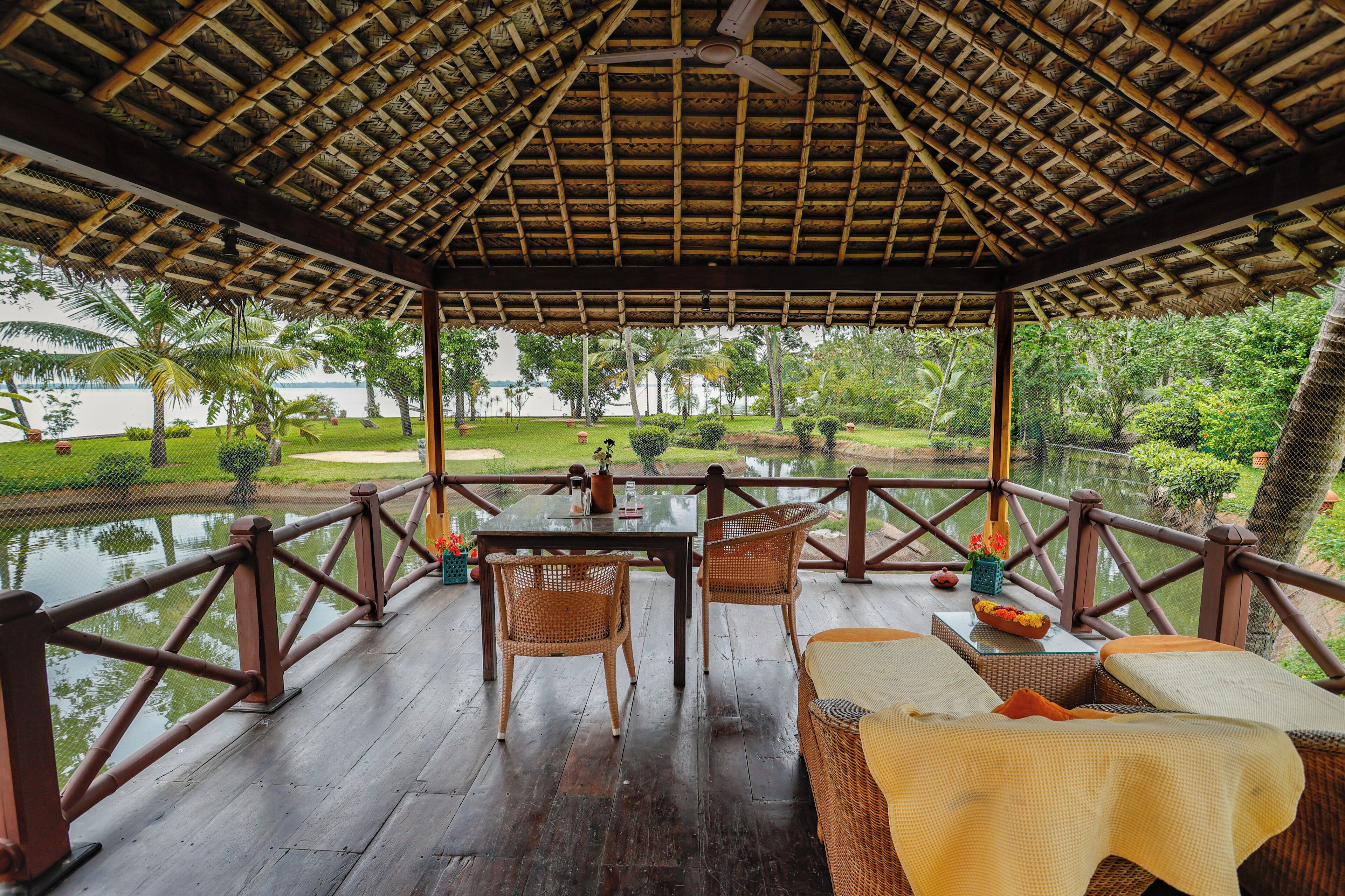 A covered outdoor seating area with a table and chairs, overlooking a body of water and greenery.