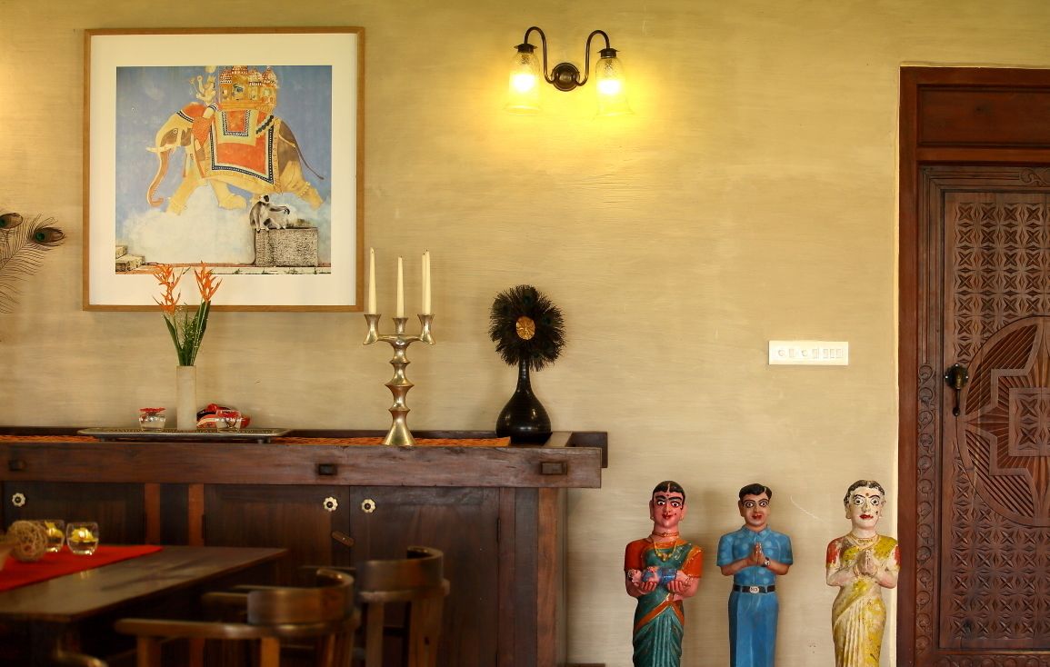 A dining area with a wooden table and chairs, a framed painting above the table, wall-mounted lights, and a decorative wall piece.