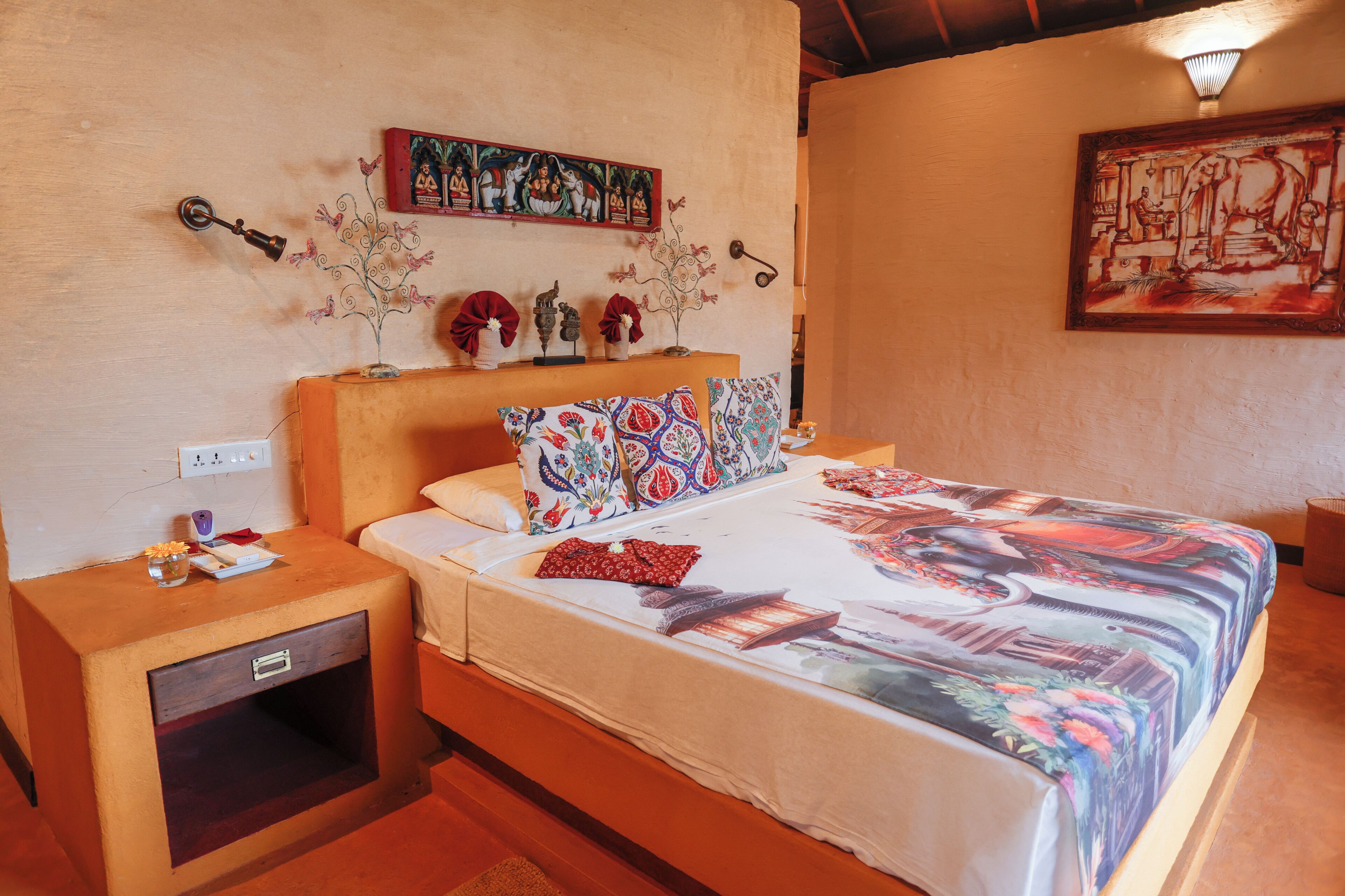 Una cama con edredón floral, una mesita de noche con lámpara y una pared con un cuadro.