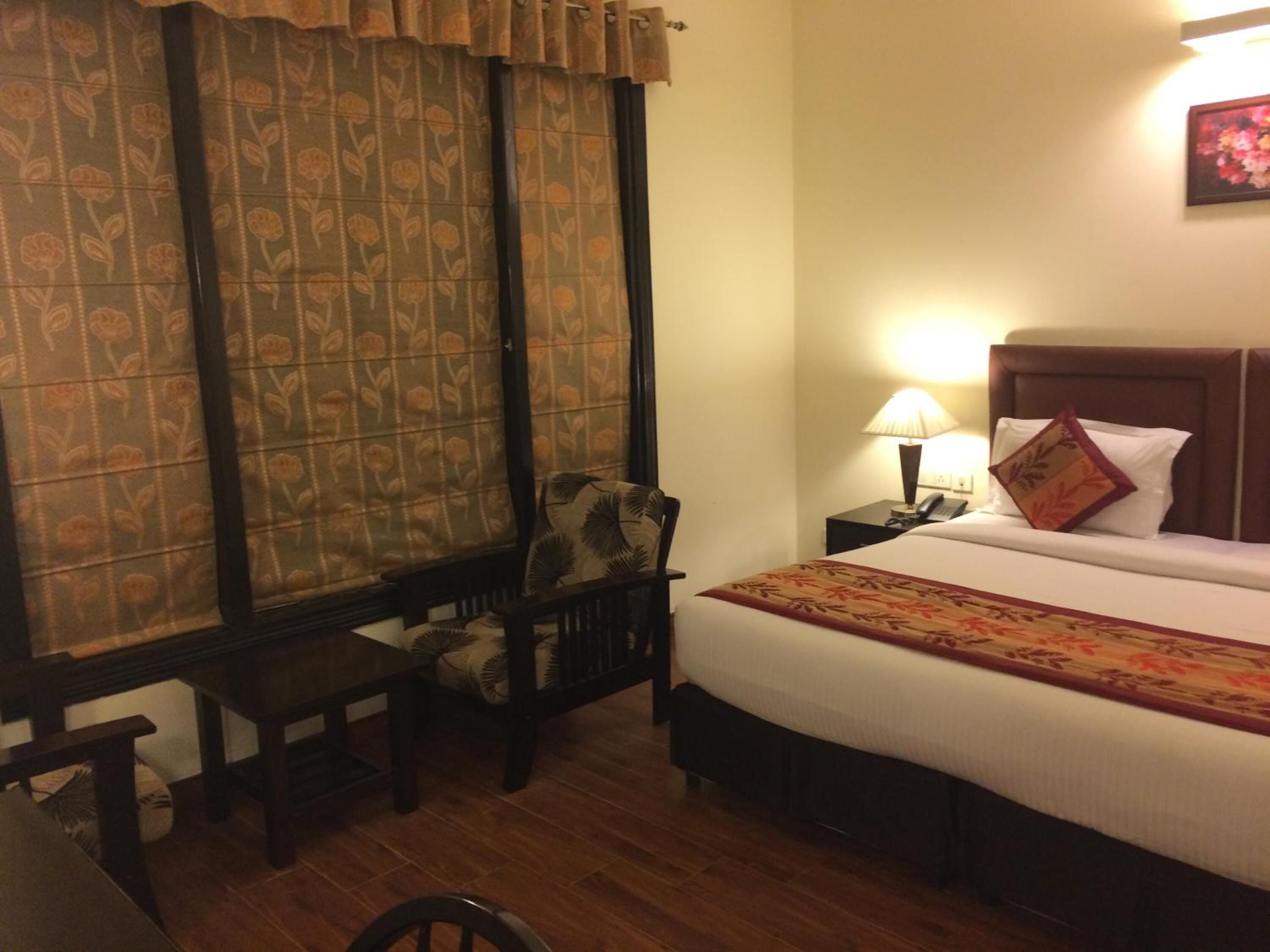 A hotel room with a bed, bedside table, lamp, chair, and curtains.