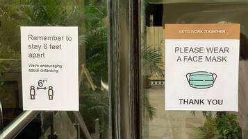 Two signs on a window: one reminding to stay 6 feet apart and another asking to wear a face mask.