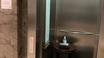An elevator with a marble wall, a hand sanitizer dispenser, and a trash bin.