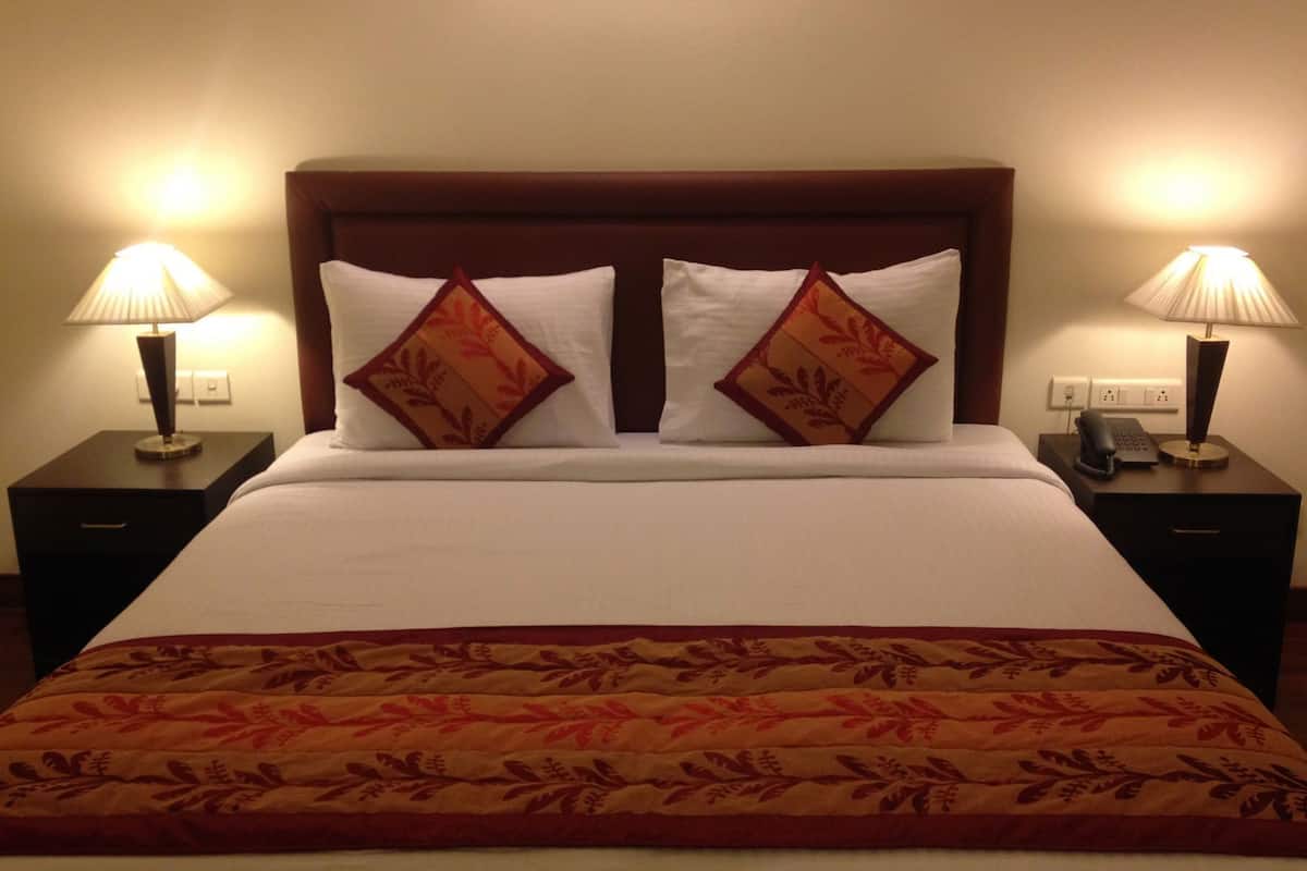 A hotel room with a large bed, two bedside lamps, a telephone, and a nightstand.