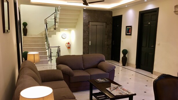 A modern living room with a sofa, a coffee table, and a lamp. There is a staircase in the background leading to an upper floor. - Hotel La Residence (Gurugram)