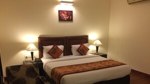 A hotel room with a large bed, two bedside lamps, a floral picture on the wall, and a patterned armchair. - Hotel La Residence (Gurugram)