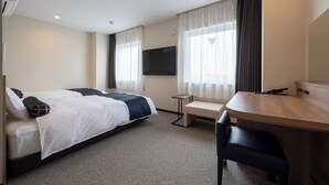 Habitación de hotel con cama, escritorio, silla, televisor y ventana con cortinas.