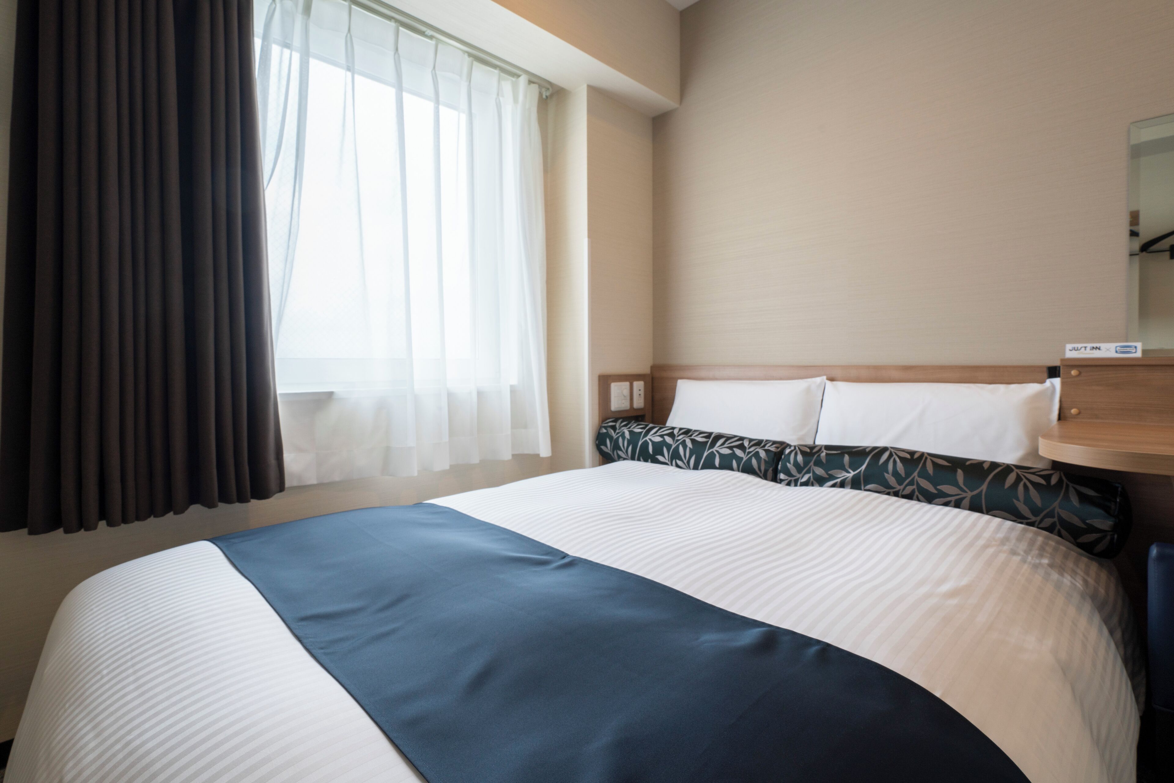 A hotel room with a large bed, a nightstand, a mirror, and a window with curtains.