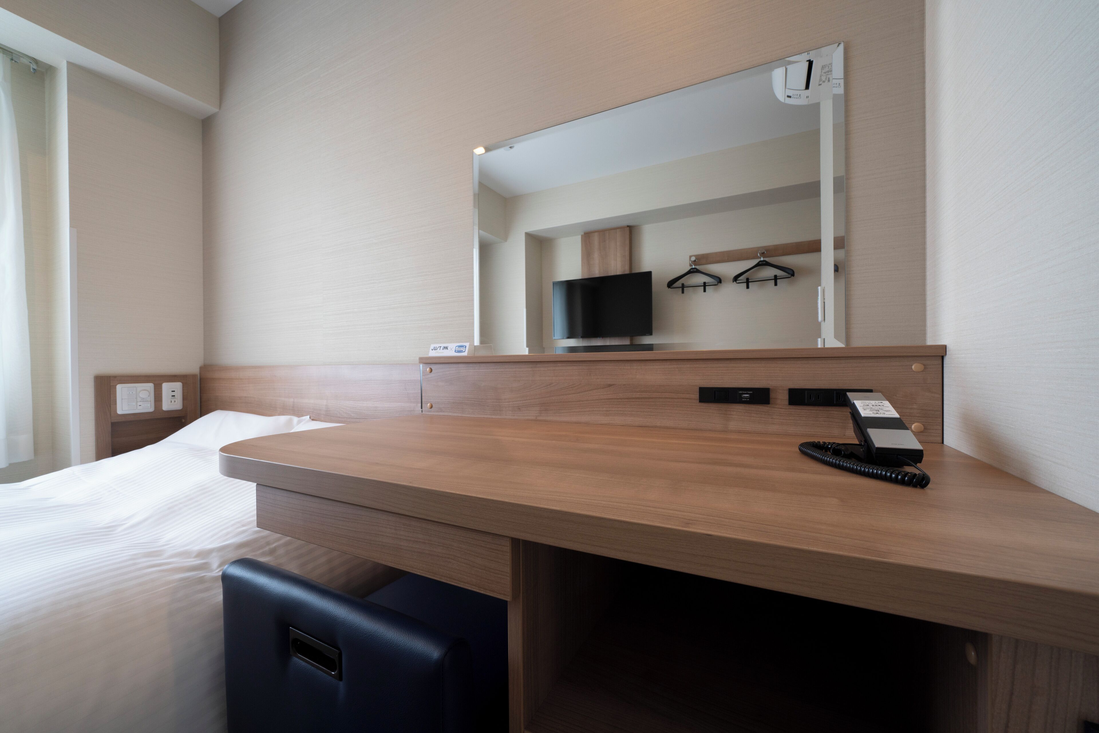 A hotel room with a wooden desk, a mirror, a television, and a telephone.
