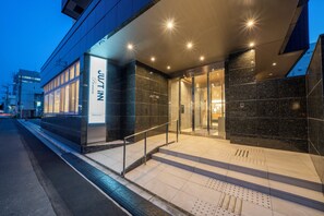 A modern hotel entrance with a glass facade, a visible staircase, and a sign reading "JUST IN." - Just Inn Premium Toyohashi Station Shinkansen Guchi (Toyohashi)