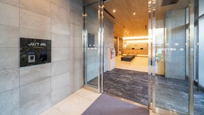 Un moderno vestíbulo de hotel con puertas de vidrio, un mostrador de recepción y un panel informativo digital.