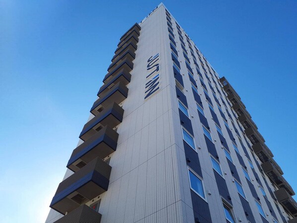 A tall, modern building with a distinctive logo on the facade. - Just Inn Premium Toyohashi Station Shinkansen Guchi (Toyohashi)