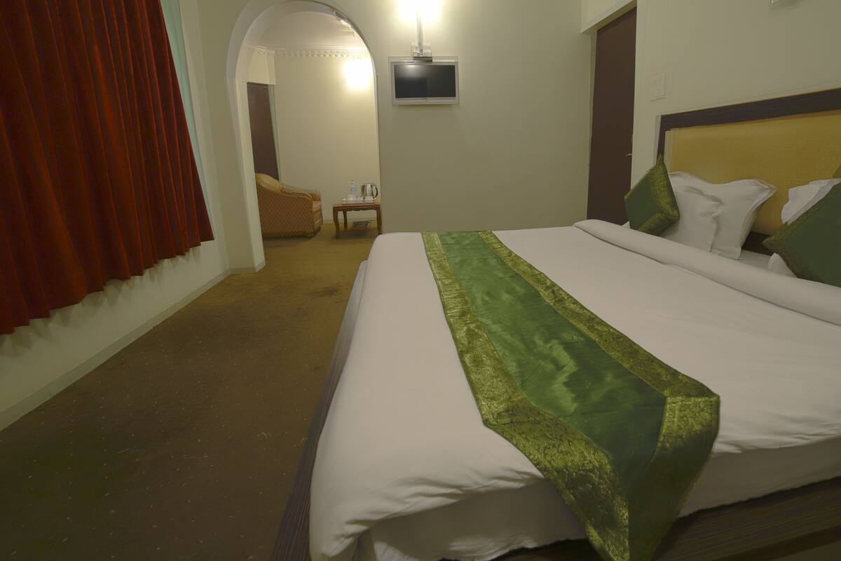 A hotel room with a bed, a television mounted on the wall, and a door leading to another room.