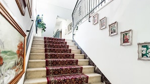 Eine Treppe mit aufwendiger, teppichbespannter Laufstufen, gerahmten Kunstwerken an den Wänden und einem Metallgeländer.