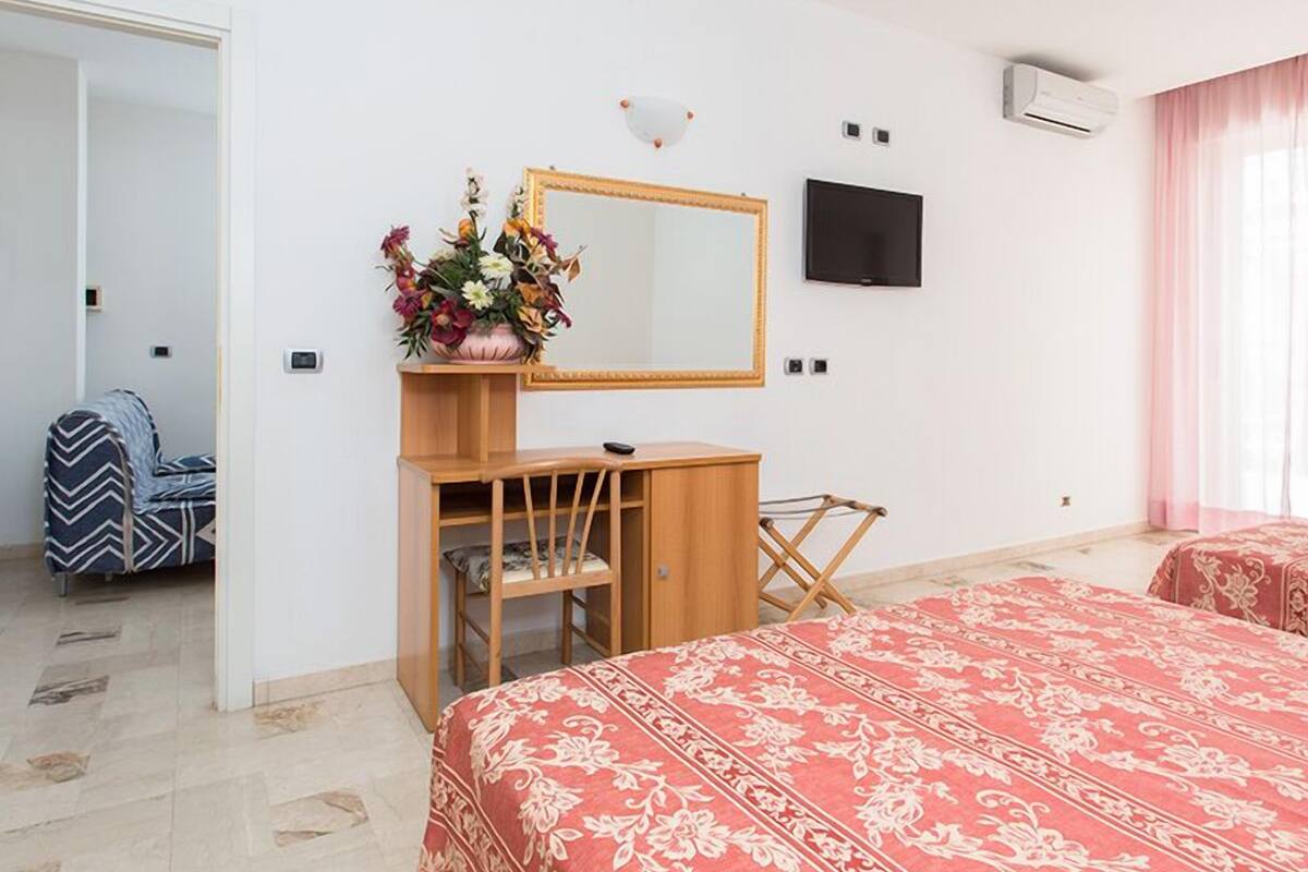 A hotel room with a bed, a desk with a mirror, a TV, and a window with curtains.