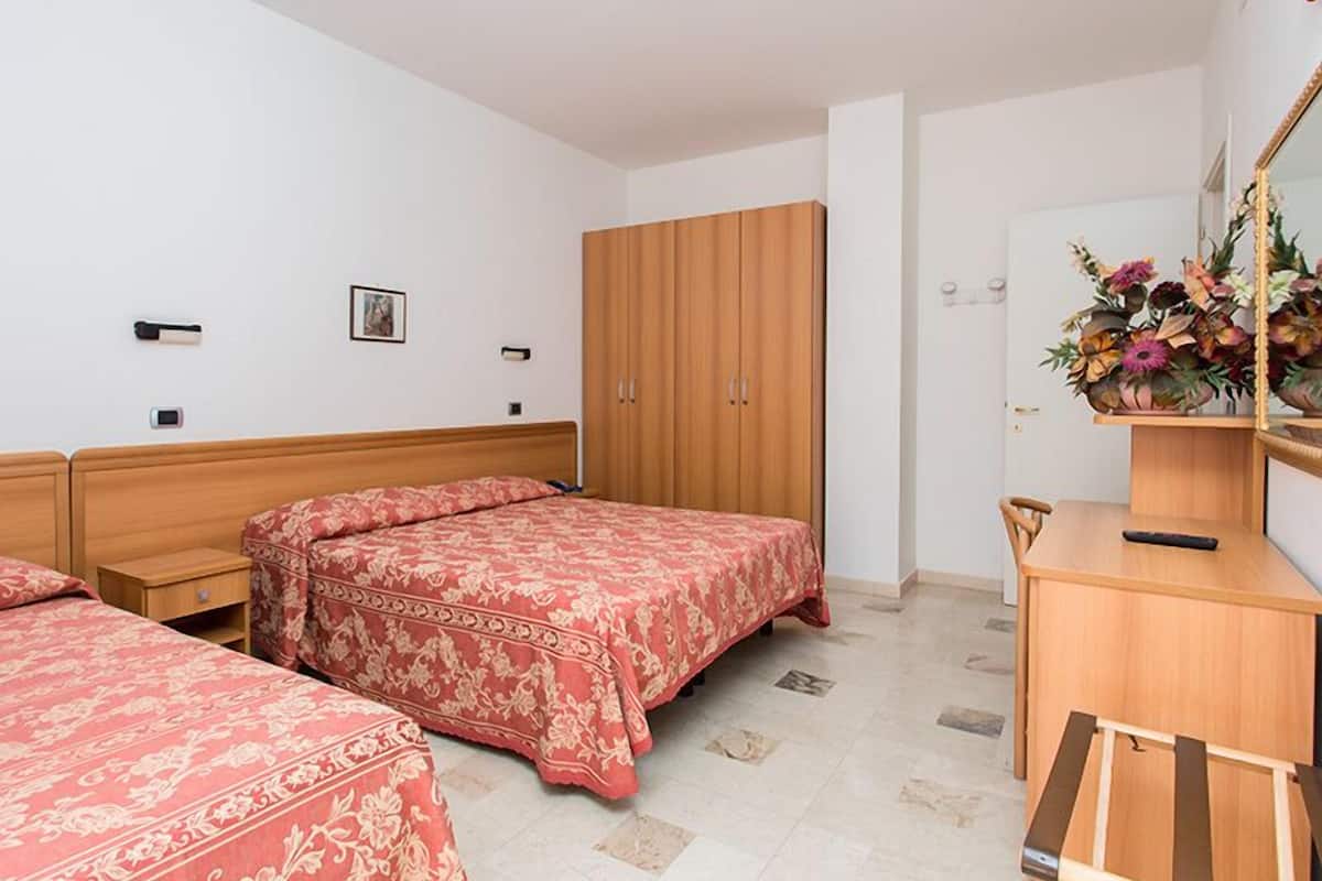 A bedroom with two beds, a wooden wardrobe, a desk, and a mirror.