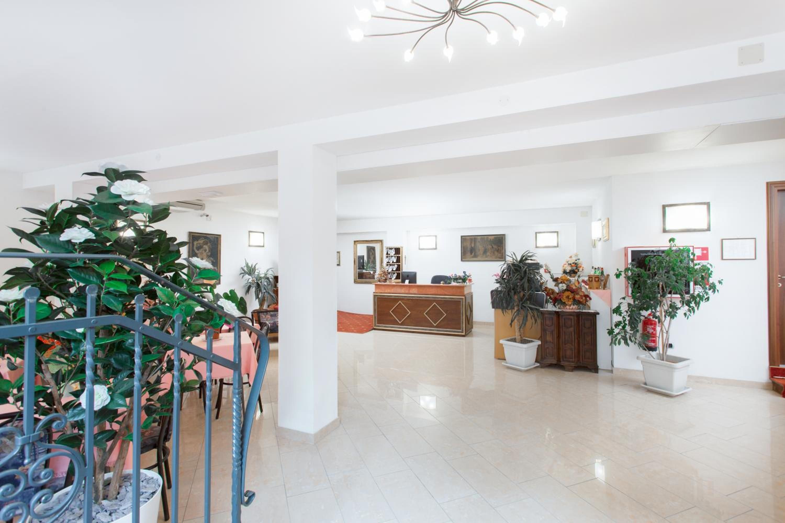 A spacious lobby with a reception desk, multiple potted plants, and a staircase with a railing.