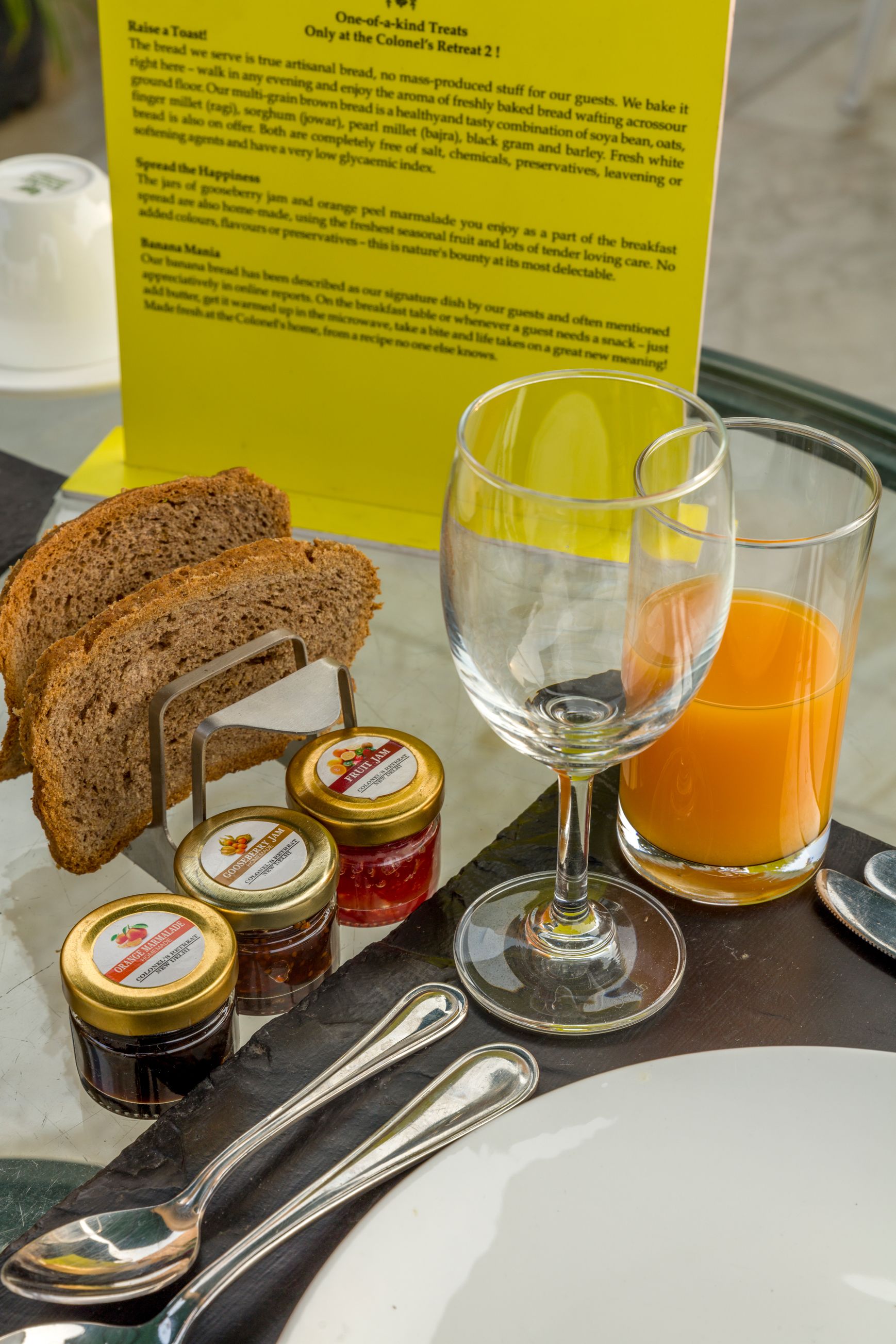 A breakfast setting with bread, a glass of orange juice, and jam jars.