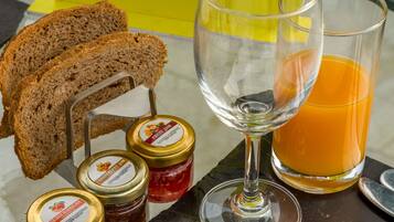 Une table mise pour le petit-déjeuner avec du pain, un verre de jus d’orange et des pots de confiture.