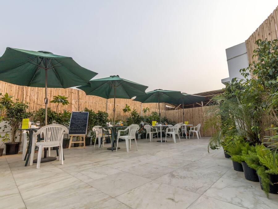 An outdoor patio with tables and chairs, green umbrellas, and potted plants.