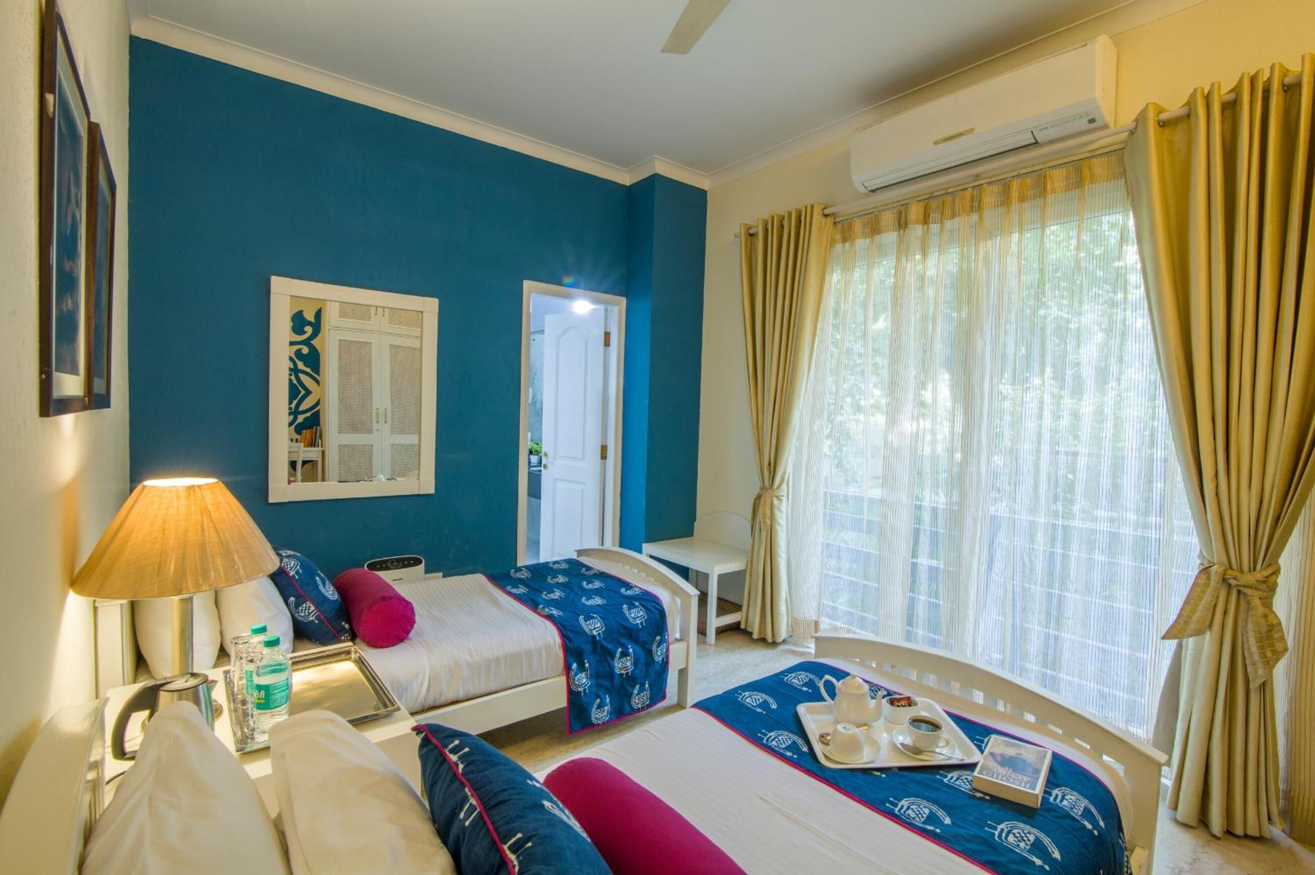 Une chambre d’hôtel avec deux lits, un bureau, une chaise, une lampe et une fenêtre avec des rideaux.