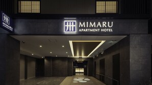 La entrada al MIMARU APARTMENT HOTEL con un diseño moderno, destacando un letrero visible y un camino limpio e iluminado hacia la entrada.
