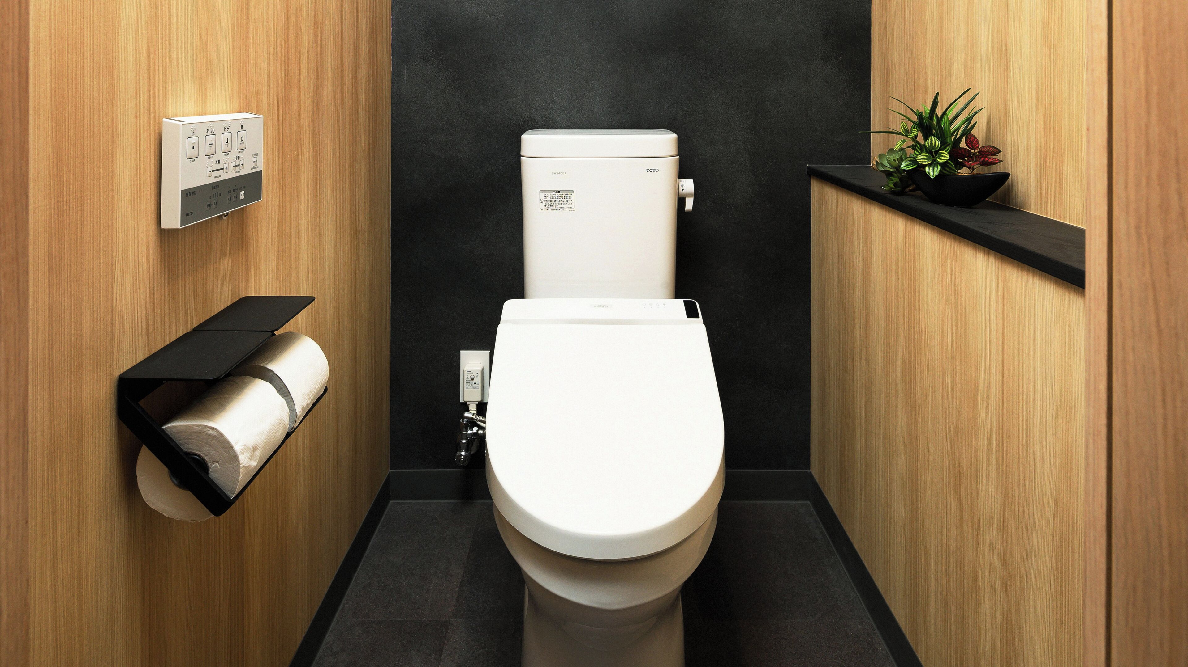A modern bathroom with a toilet, a toilet paper holder, and a small shelf with plants.