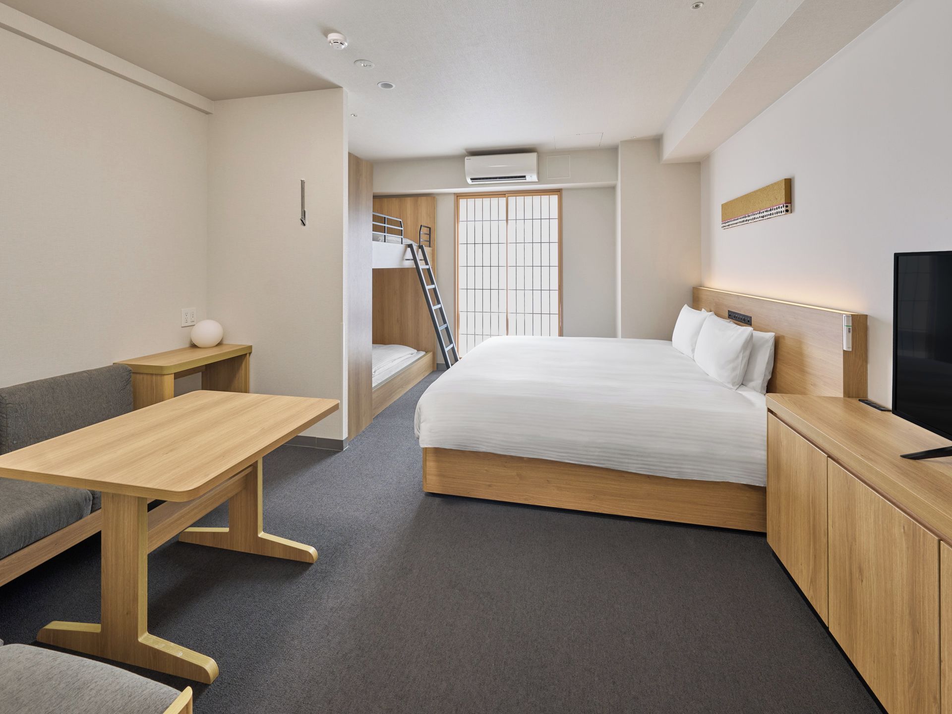 A compact hotel room with a bunk bed, a desk, a television, and a small seating area.