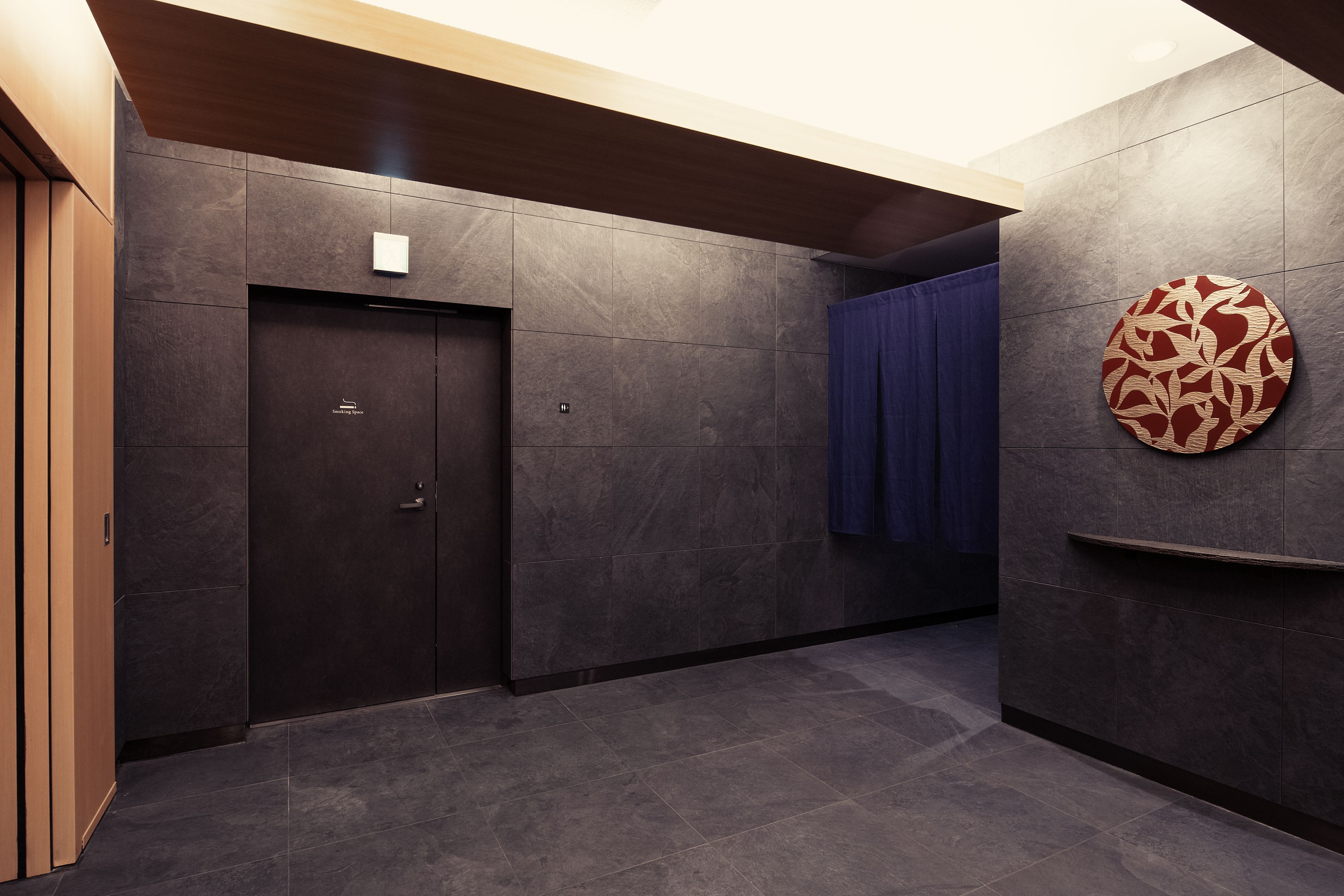 A modern hallway with dark tiled walls, a wooden door, and a blue curtain.