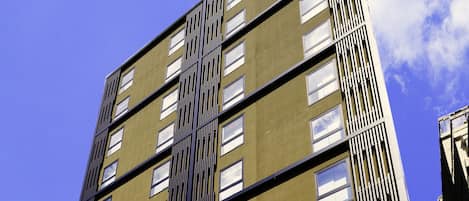 Un moderno edificio a più piani con facciata gialla ed elementi verticali neri, con la scritta "MIMARU APARTMENT HOTEL".
