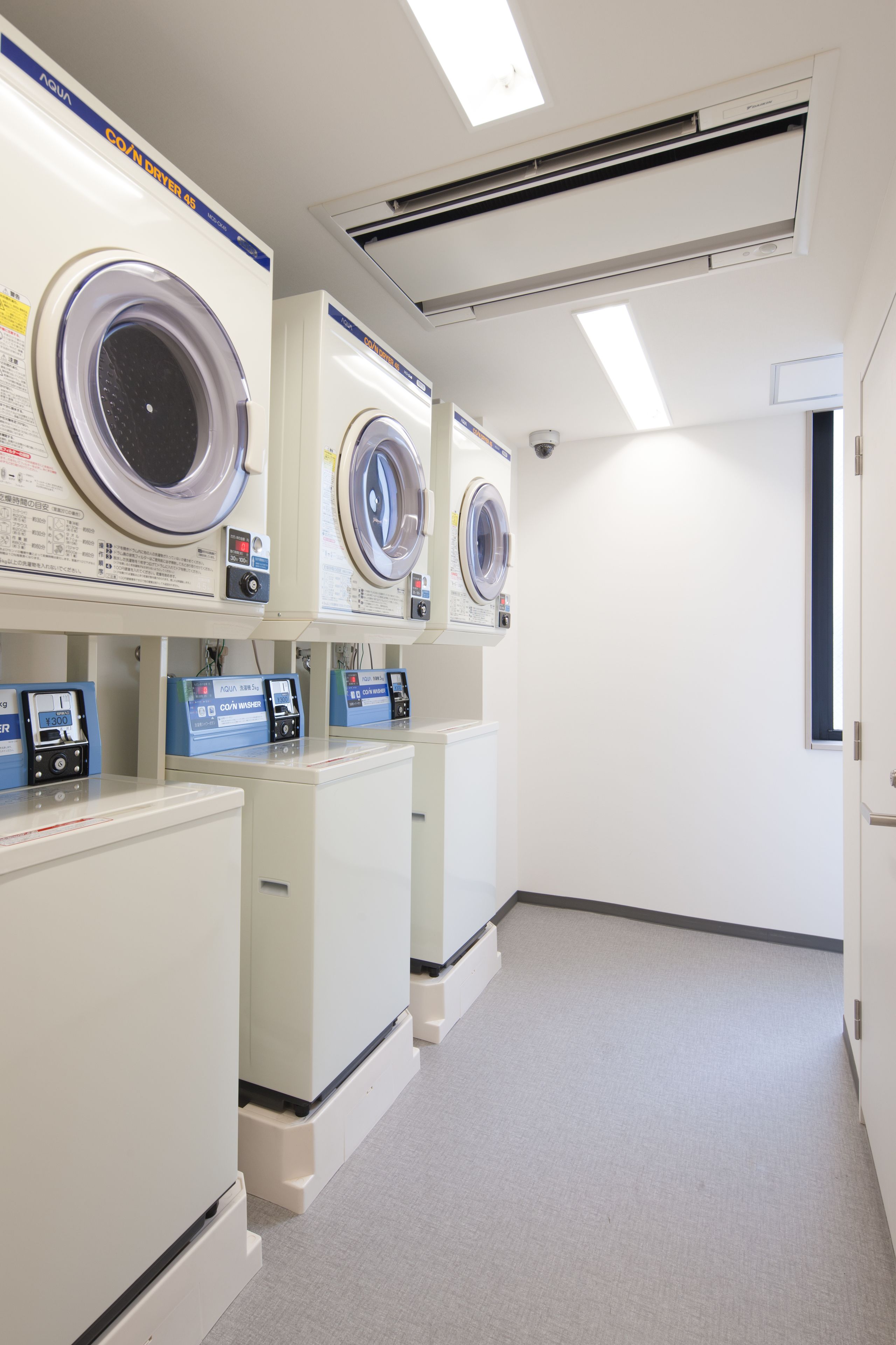 Une laverie équipée de plusieurs machines à laver et de plusieurs séchoirs, d’un panneau de commande et d’un système de ventilation.