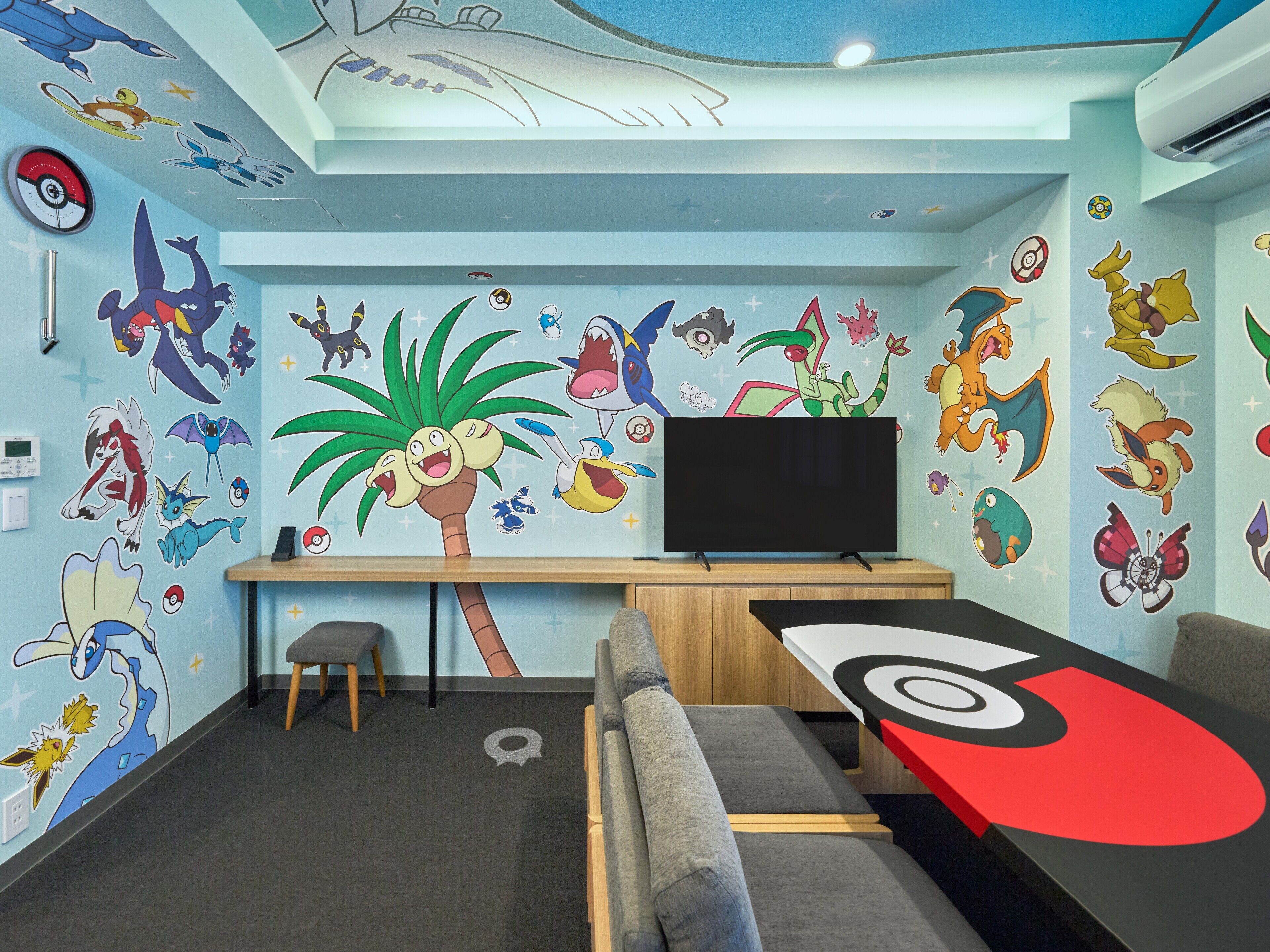 A room with a TV, a desk, a chair, and a couch. The walls are decorated with cartoon characters.