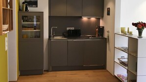 A compact kitchen with a built-in oven, a sink, and a countertop. There is a small cabinet with a glass door and a shelf with decorative items. - Bergblick Riedlern, Kreuth Riedlern - Mountain View Riedlern - Apartment (Kreuth)