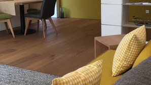 A compact living space with a dining area, a sofa with checkered cushions, a white refrigerator, and a shelf with decorative items. - Bergblick Riedlern, Kreuth Riedlern - Mountain View Riedlern - Apartment (Kreuth)